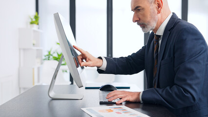 Middle-aged white man in a suit working in the office with desktop PC.