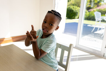 Happy african american boy practicing sign language in sunny living room at home
