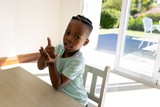 Happy african american boy practicing sign language in sunny living room at home