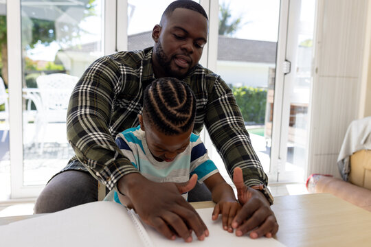 Sight impaired african american father and son practicing reading braille together at home