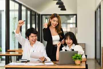 Happy businesspeople looking at laptop screen and making yes gesture, celebrating their project success