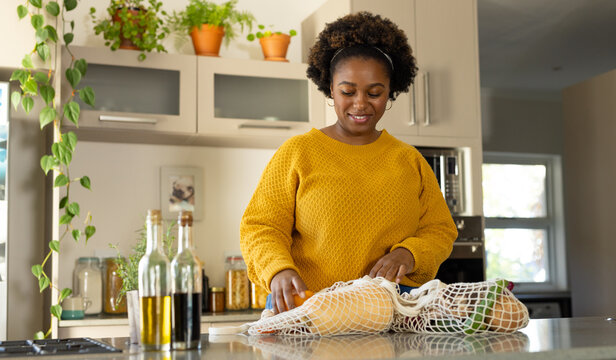 Happy plus size african american woman unpacking groceries in kitchen - Powered by Adobe