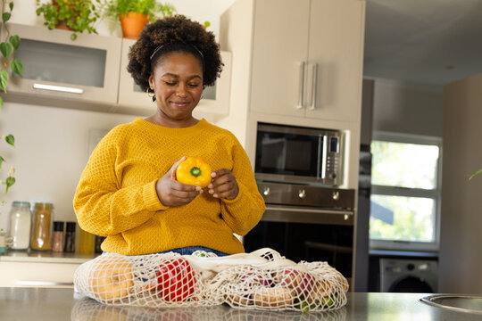 Happy plus size african american woman unpacking groceries in kitchen