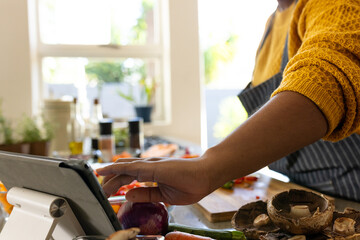 Midsection of plus size african american woman in apron preparing meal using tablet in kitchen