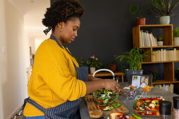 Plus size african american woman in apron preparing meal using tablet in kitchen