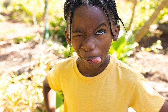 Naklejki African american boy wearing yellow t-shirt, making funny face in garden