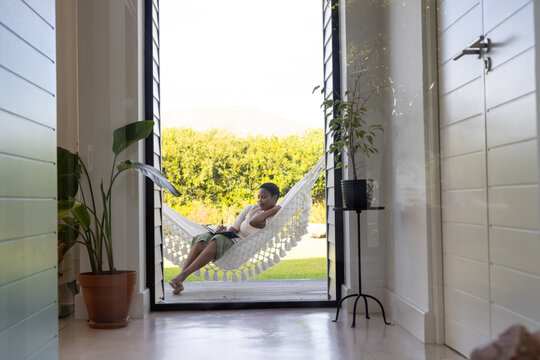 Happy african american woman writing in notebook sitting in hammock on terrace, copy space