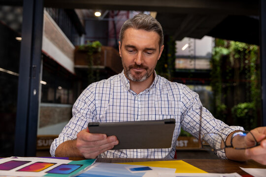 Caucasian businessman holding glasses using a digital tablet at modern office