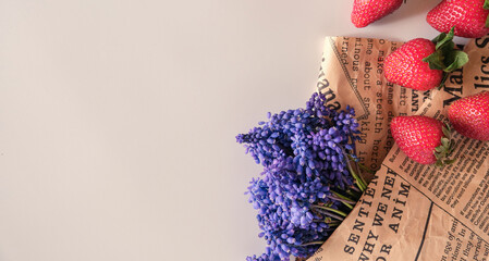 Red fresh strawberry and purple muscari flower with an vintage newspaper on white background, with copy space for text