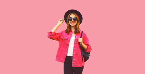 Portrait of stylish modern smiling young woman wearing jacket, black round hat and backpack on pink background