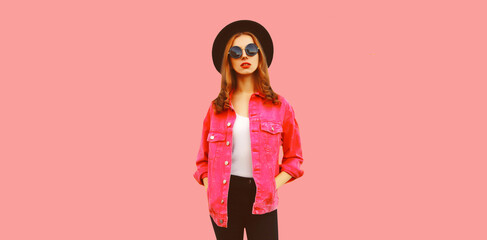 Portrait of stylish modern young woman wearing jacket, black round hat on pink background