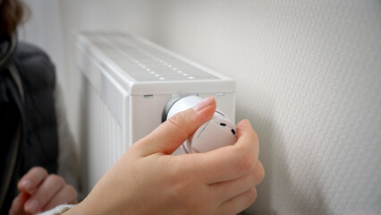 Closeup of woman adjusting heating radiator thermostat and warming her hands. Concept of energy crisis, high bills, broken heating system, economy and saving money on monthly utility payments.