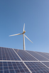 Solar panels and wind turbine against blue sky