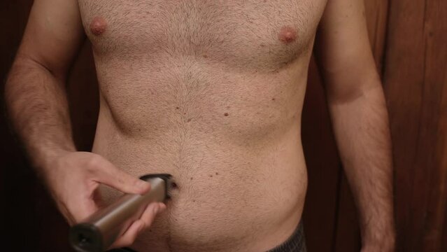 Unrecognizable topless man cuts his black thick hair on chest and stomach with an electric machine. Concept of high body hair. 4K