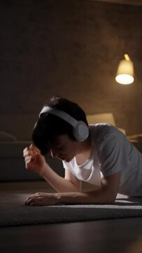 Cute teenager boy listening to music on headphones and dancing while lying on the floor at night