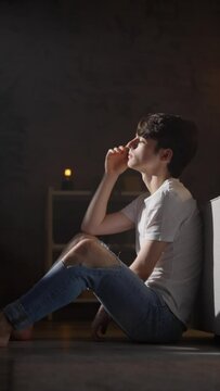 Sad teenager boy sitting on the floor at night. Depression, loneliness and adolescence problems concept. Young person overthinking