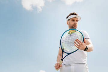 healthy lifestyle, handsome man in active wear and visor cap holding tennis racquet on court