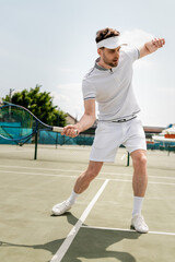 sporty man in sports visor holding racket and playing tennis on court, training and motivation