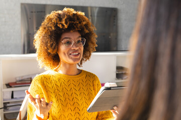 Happy biracial female colleagues with tablet discussing work in office