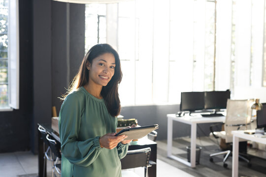 Portrait of happy biracial casual businesswoman using tablet in office