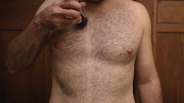 Unrecognizable topless man cuts his black thick hair on chest and stomach with an electric machine. Concept of high body hair. 4K