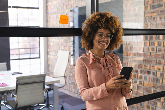 Portrait of happy biracial casual businesswoman using smartphone in office