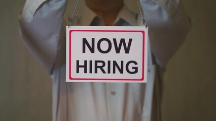 Now hiring sign posted on business door. A man pins a Now Hiring sign on the glass door. Employment concept