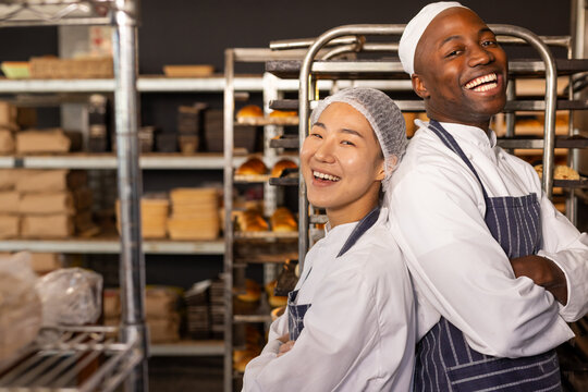 Portrait of happy diverse bakers wearing aprons in bakery with arms crossed