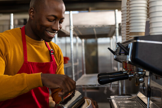 Happy african american male bakery worker wearing red apron and preparing coffee