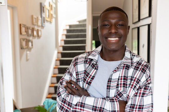 Portrait of happy african american man leaning on door frame and smiling at home, copy space