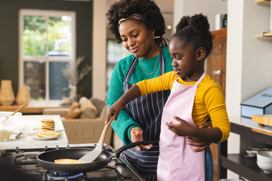 Happy african american mother and daughter baking pancakes in kitchen at home