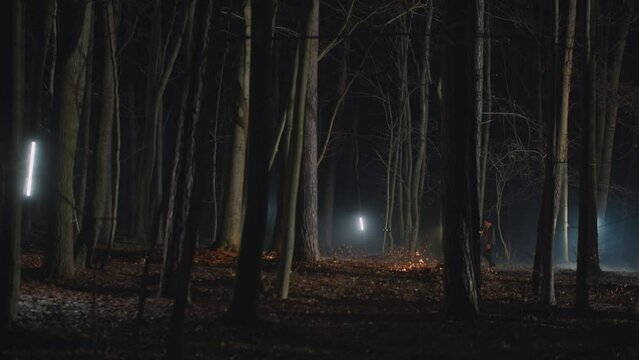 Two males walking in the night autumn forest with flashlights. Young detectives searching clues in crime scene. Footsteps kick up fallen leaves, naked woods, lighting lamps, far view