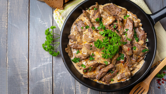 delicious beef stroganoff - veal strips stewed with porcini in sour cream sauce sprinkled with finely chopped parsley on skillet, authentic recipe, view from above