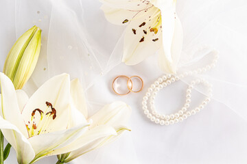 Top view of two gold wedding rings on a white bridal bridal veil and pearl beads. delicate white lilies. the concept of a wedding card,