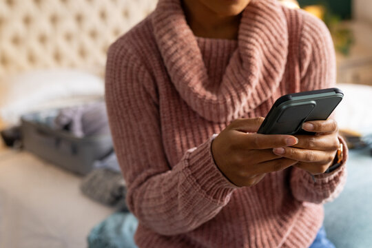 Midsection of biracial woman using smartphone in bedroom