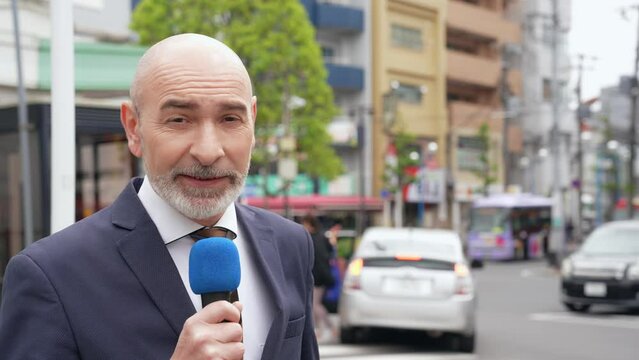 A Caucasian male reporter broadcasting on television in a local city.