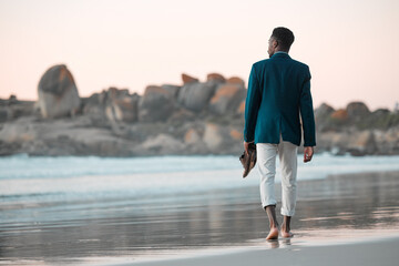 Walking, beach and back of business man for journey on holiday, vacation and freedom by ocean. Professional, travel and male entrepreneur barefoot for calm, peace and relaxing in nature at sunset