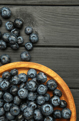 Fresh blueberry in wooden bowl on black background. Concept of healthy and dieting eating. Vertical photo