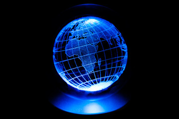 World map model engraved with a laser inside a glass globe. World map with blue neon light on isolated black background. Asian and African continents are in the foreground. Earth and finance concept.