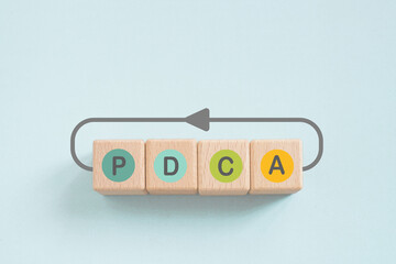 PDCA text in color circle ,means Plan Do Check Act, on wooden cube block with loop line on grunge...