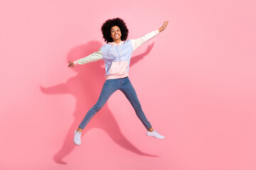 Full length photo of funky excited little child dressed hoodie jumping high arms sides isolated pink color background