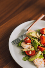 Vegetable salad with nuts on a white plate with a cup of coffee.