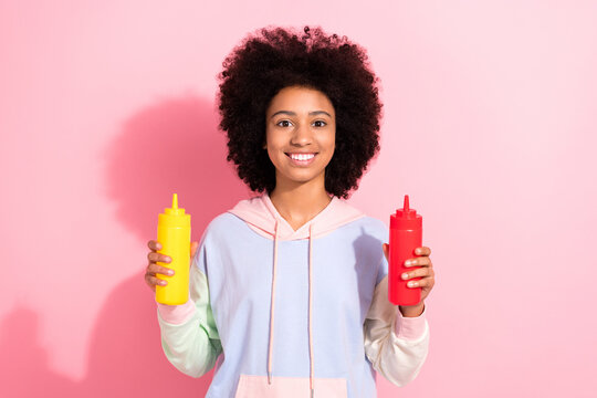 Photo of positive cheerful small kid wear sweatshirt holding two sauce bottles isolated pink color background