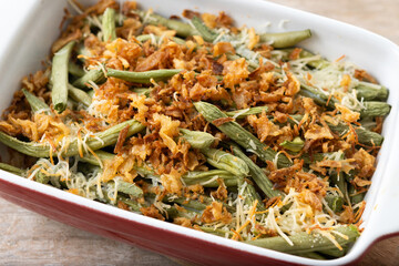 A traditional green bean casserole topped with French Fried Onions and cream of mushroom on wooden table. Close up