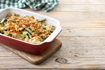 A traditional green bean casserole topped with French Fried Onions and cream of mushroom on wooden...