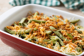 A traditional green bean casserole topped with French Fried Onions and cream of mushroom on wooden table
