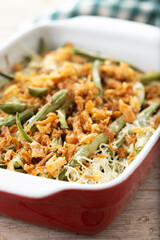 A traditional green bean casserole topped with French Fried Onions and cream of mushroom on wooden table. Close up