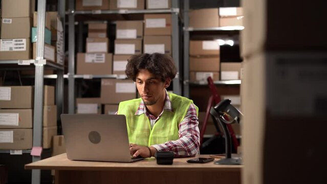 Arab male warehouse worker uses laptop to work with database