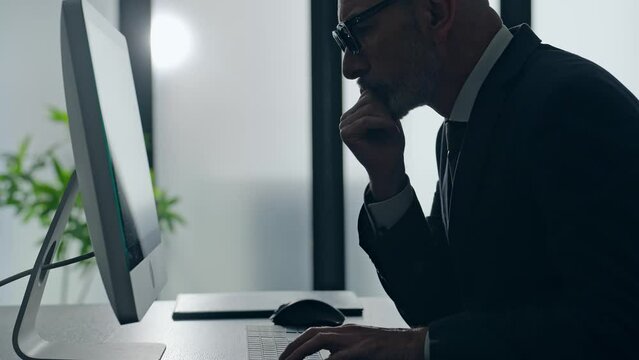 Middle-aged white man in a suit working in the office with desktop PC.