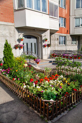 Fototapeta na wymiar Flowerbeds of bright flowers and various plants in front of the entrance of a residential building. Agriculture Landscaping landscaping of cities.